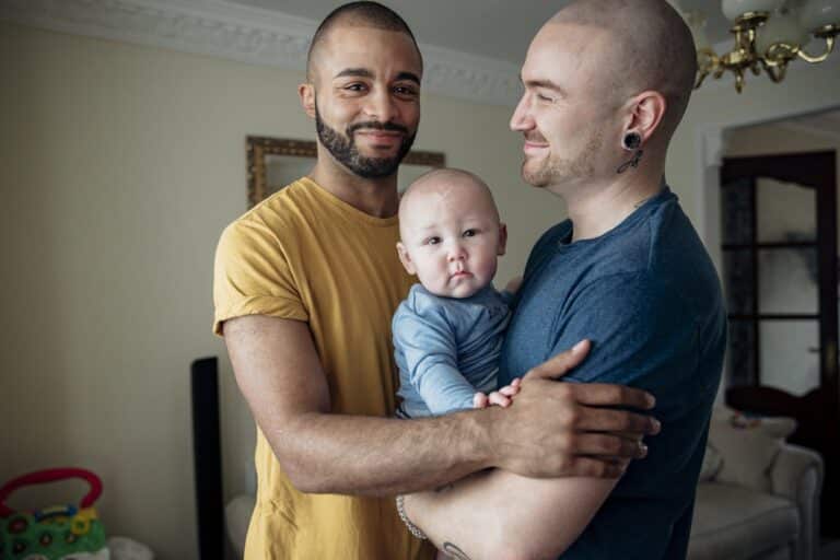 Two men spending time with their little baby boy. They're all together at home standing in an embrace