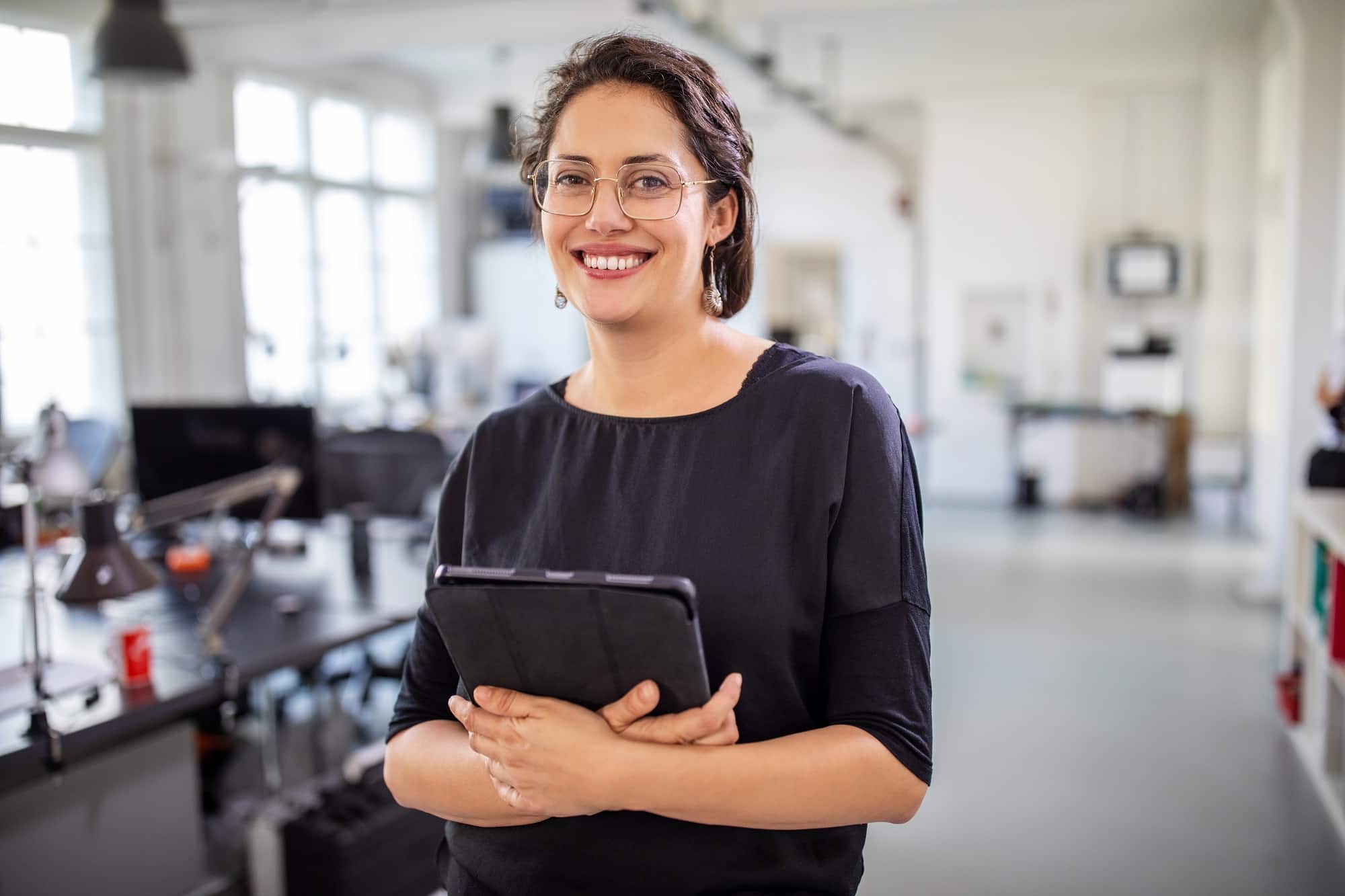 Portrait of a mature businesswoman holding a digital tablet in office. Smiling female professional standing at modern workplace.