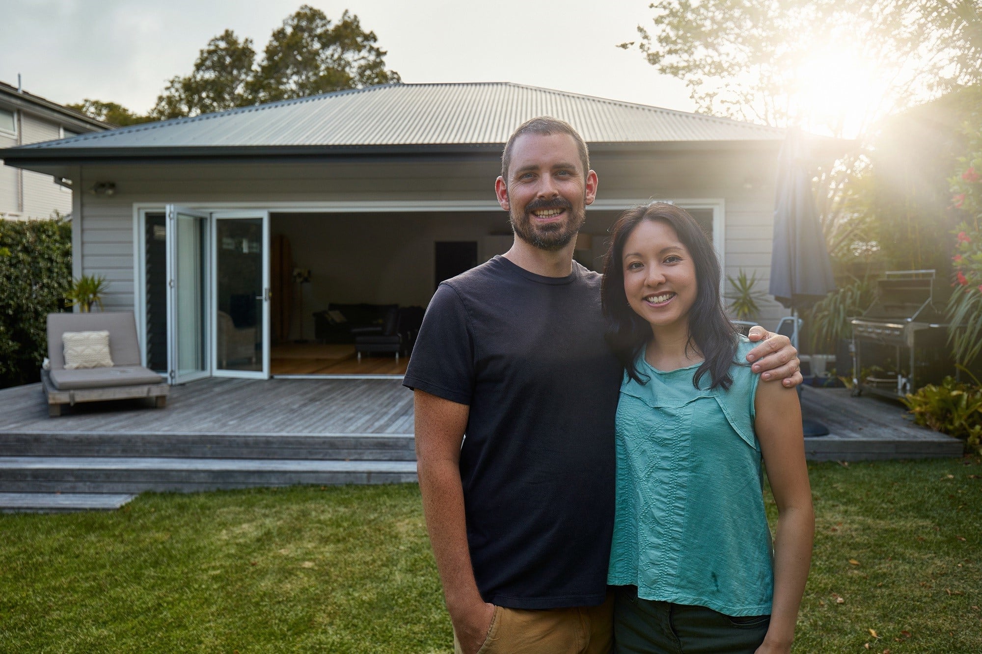 Portrait of smiling mid adult couple standing against house during sunset. Happy man and woman are in lawn at back yard. They are in casuals.
